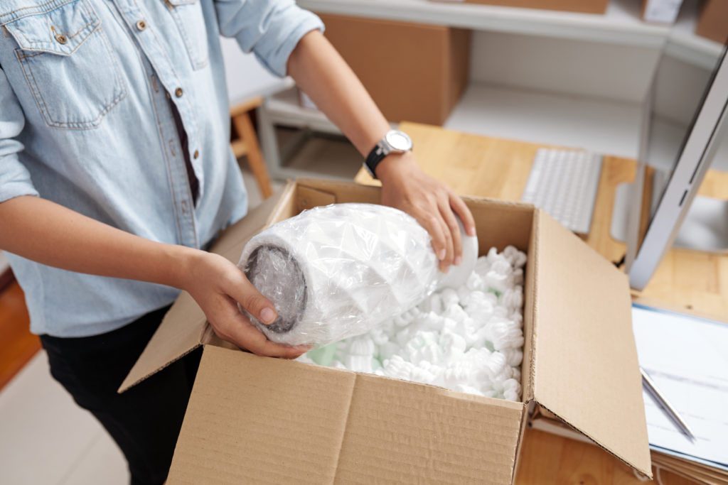 Post office worker packing vase in box for delivery