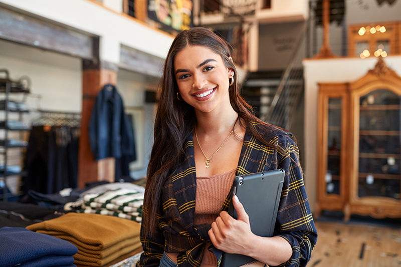 International Shipping: woman holding tablet in clothing store preparing to ship items internationally